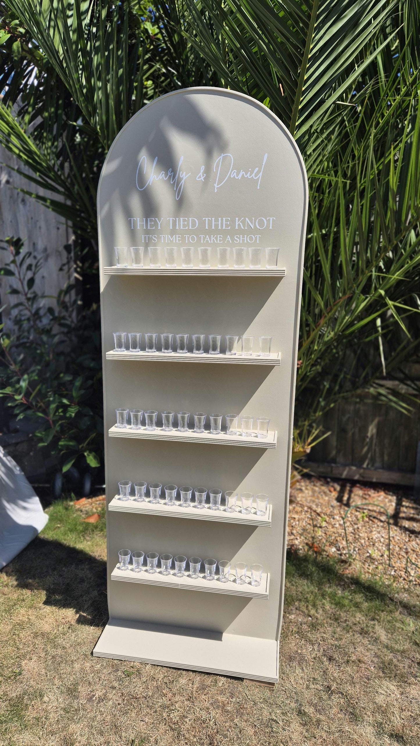 full front view of a wedding shot wall outside in a garden party setting with glasses
